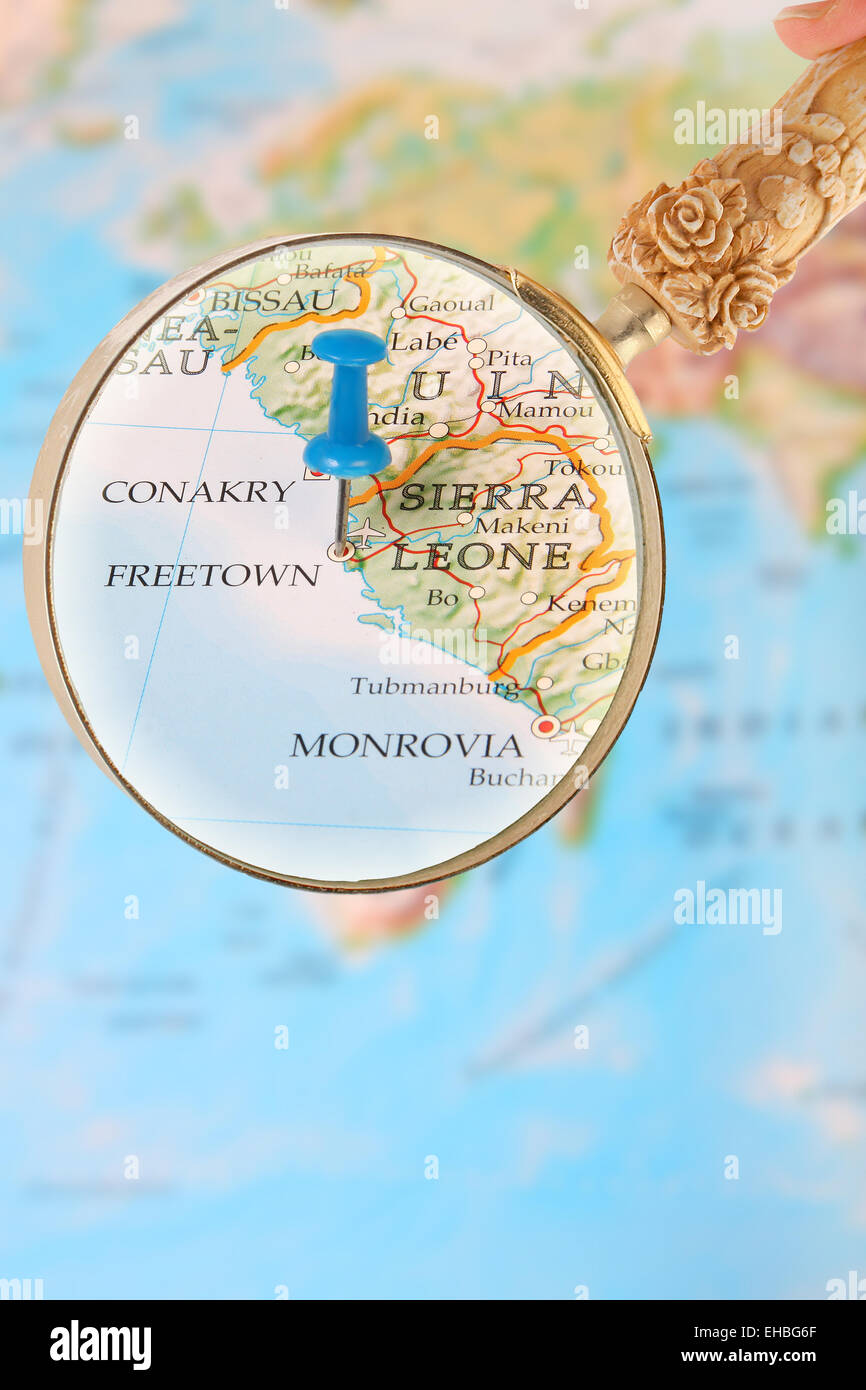 Blue tack on map of Africa with magnifying glass looking in on Freetown, Sierra Leone Stock Photo