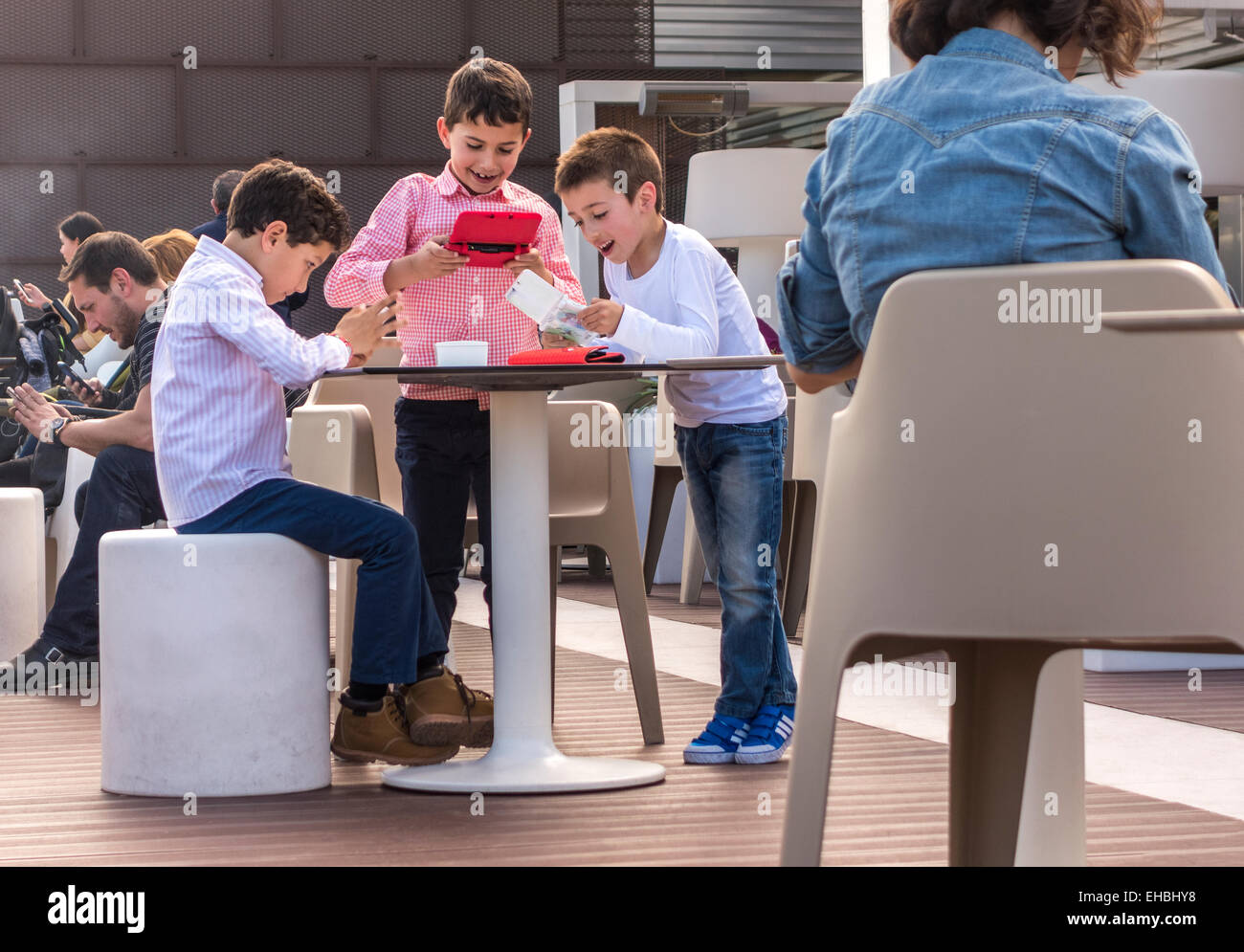 Children playing handheld computer games while grown ups, parents, are all looking at their smartphones on a Sunday afternoon Stock Photo