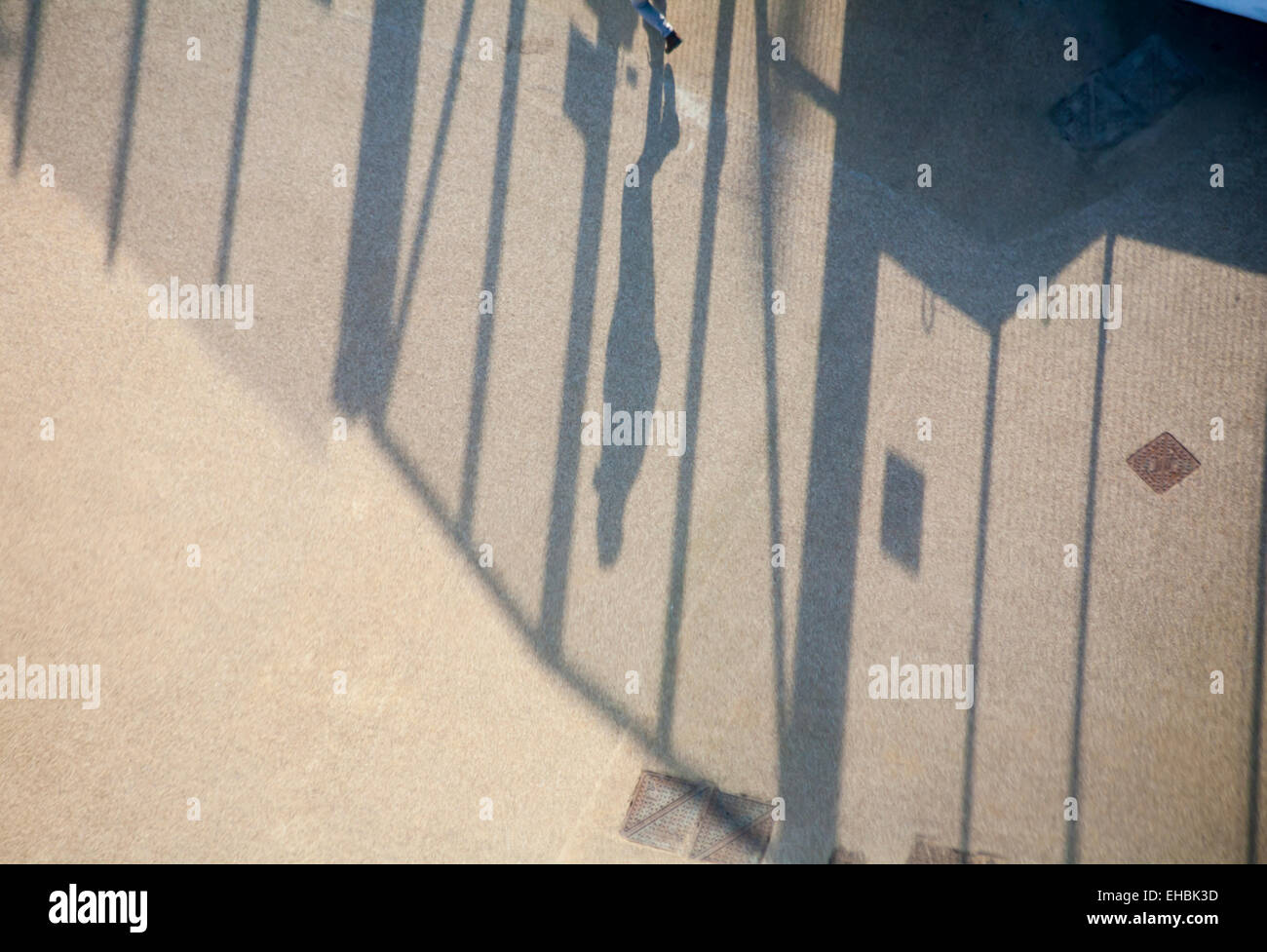 Looking down at feet with shadow of figure walking along fencing Stock Photo