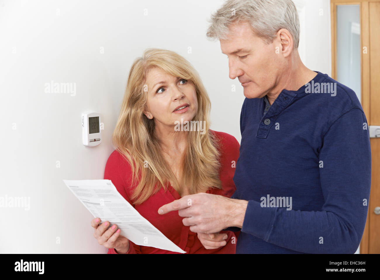Worried Mature Couple With Bill Turning Down Central Heating Stock Photo