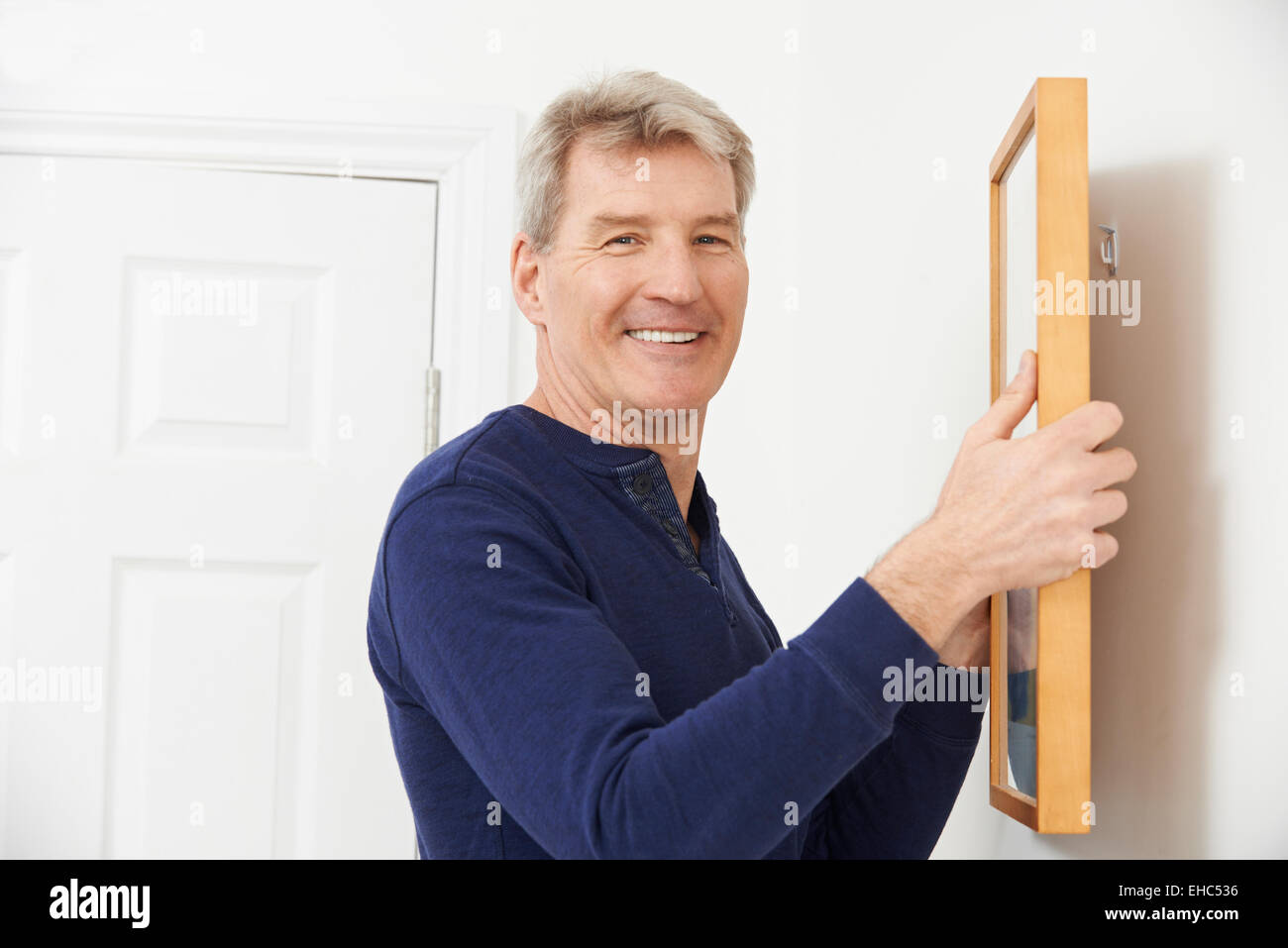 Mature Man Hanging Picture On Wall Stock Photo