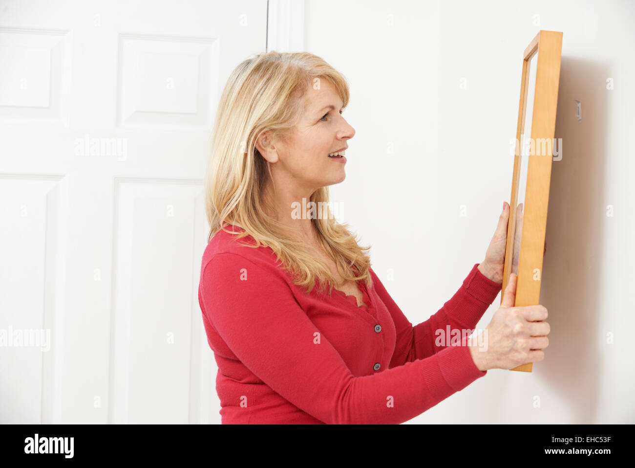 Mature Woman Hanging Picture On Wall Stock Photo