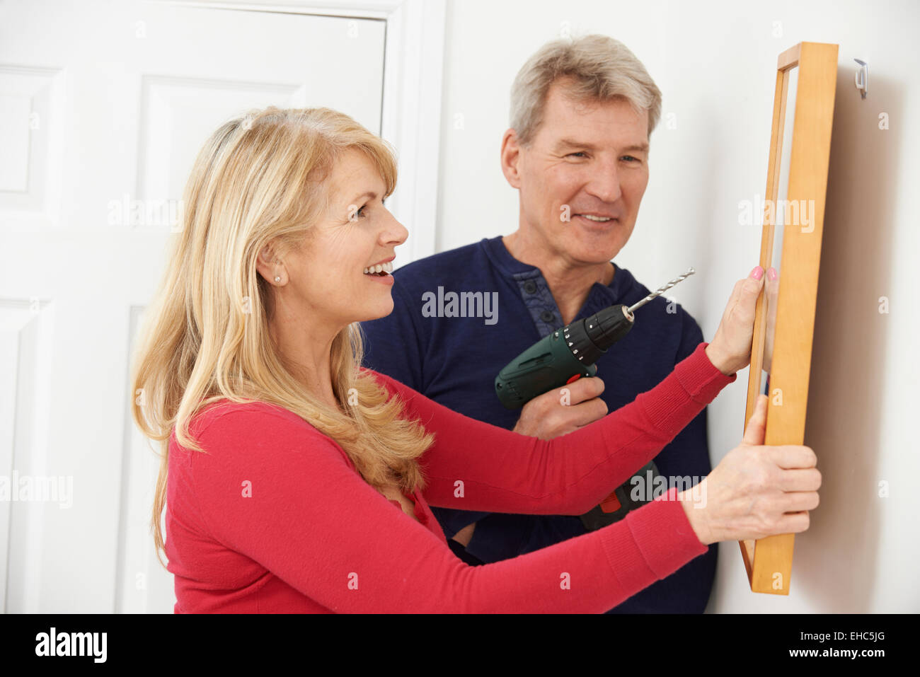 Mature Couple Drilling Wall To Hang Picture Frame Stock Photo