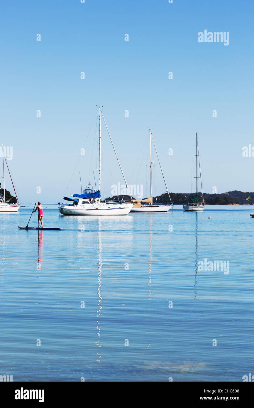 Woman paddle-boarding by yachts in sea Stock Photo