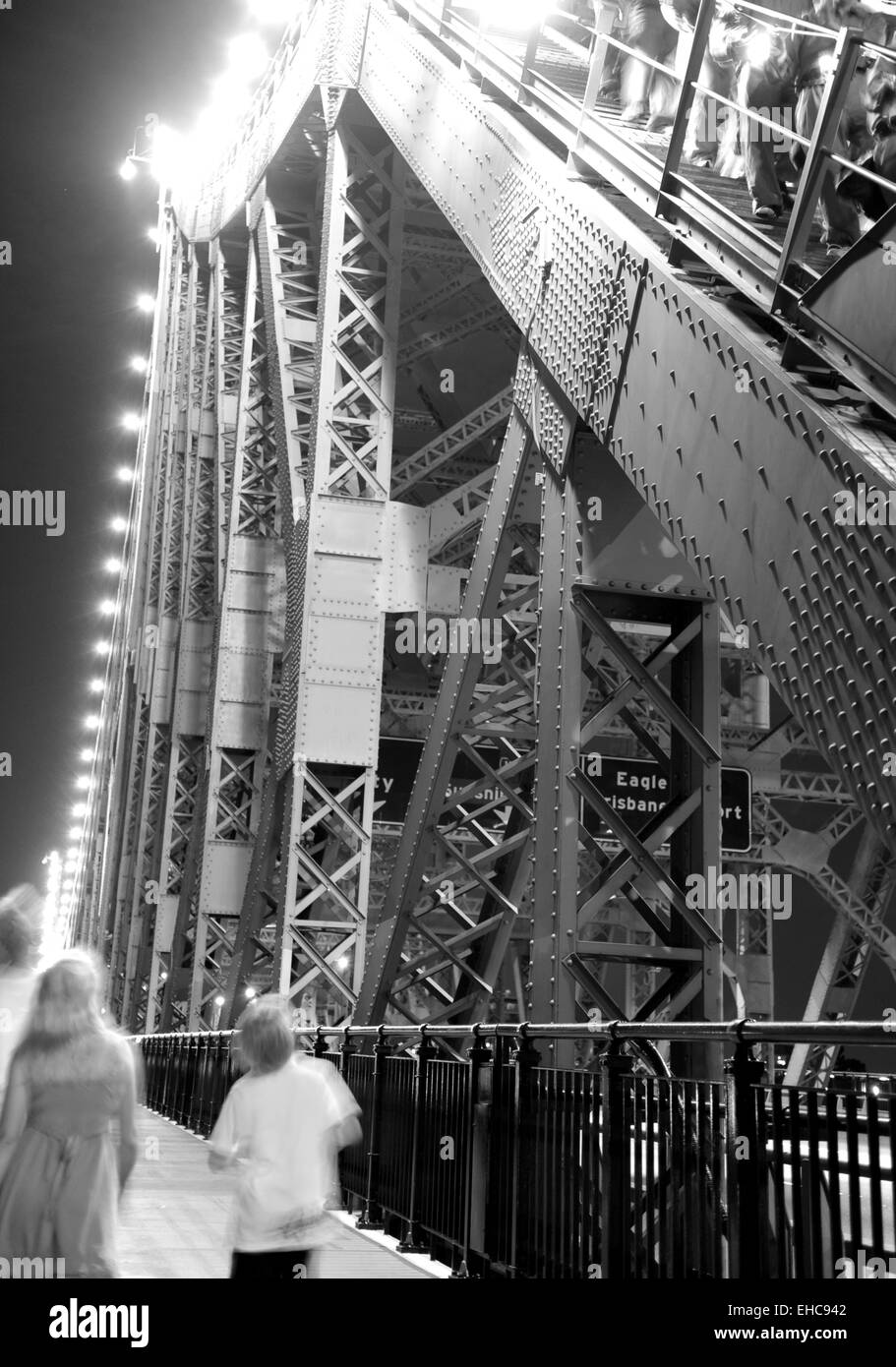 Pedestrians walking next to the Story Bridge and its framework of steel girders and rivets.  Located in Brisbane, Australia Stock Photo
