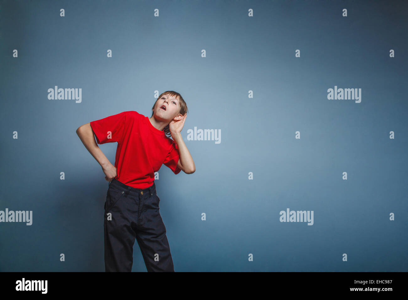 Boy, teenager, twelve years a in  red shirt holding his ear hand Stock Photo