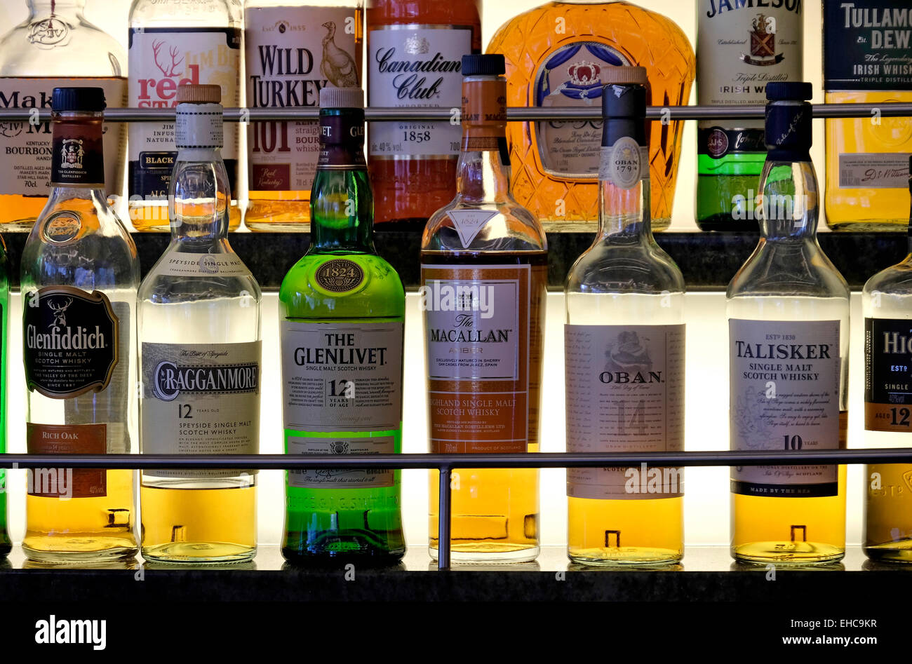 Selection of Whiskeys and other Alcoholic Spirits on a Lit Glass Shelf Stock Photo