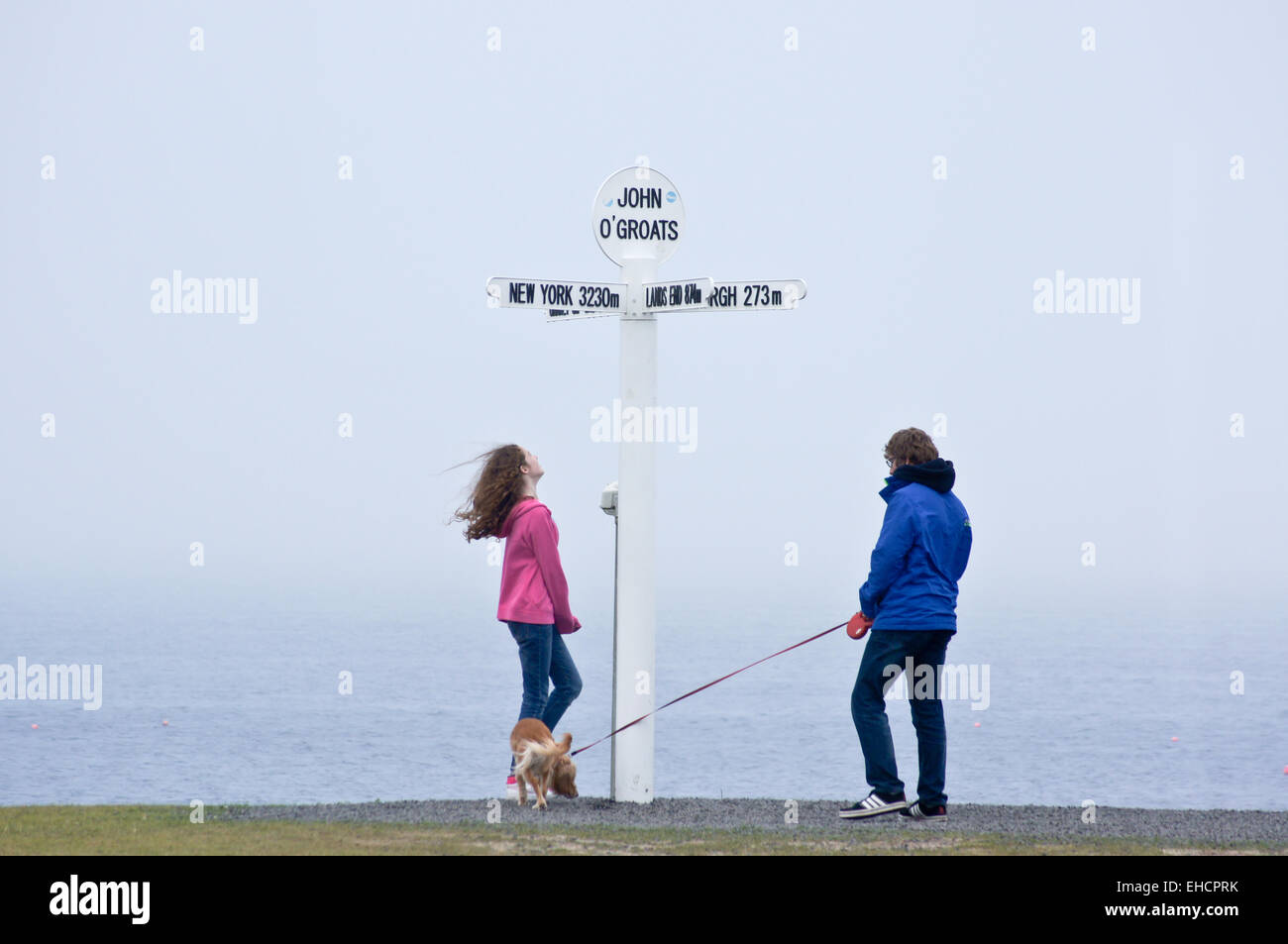 Walkers passing the sign showing distances to Land's End, John O'Groats, Caithness, Scotland, with a dog on a lead Stock Photo