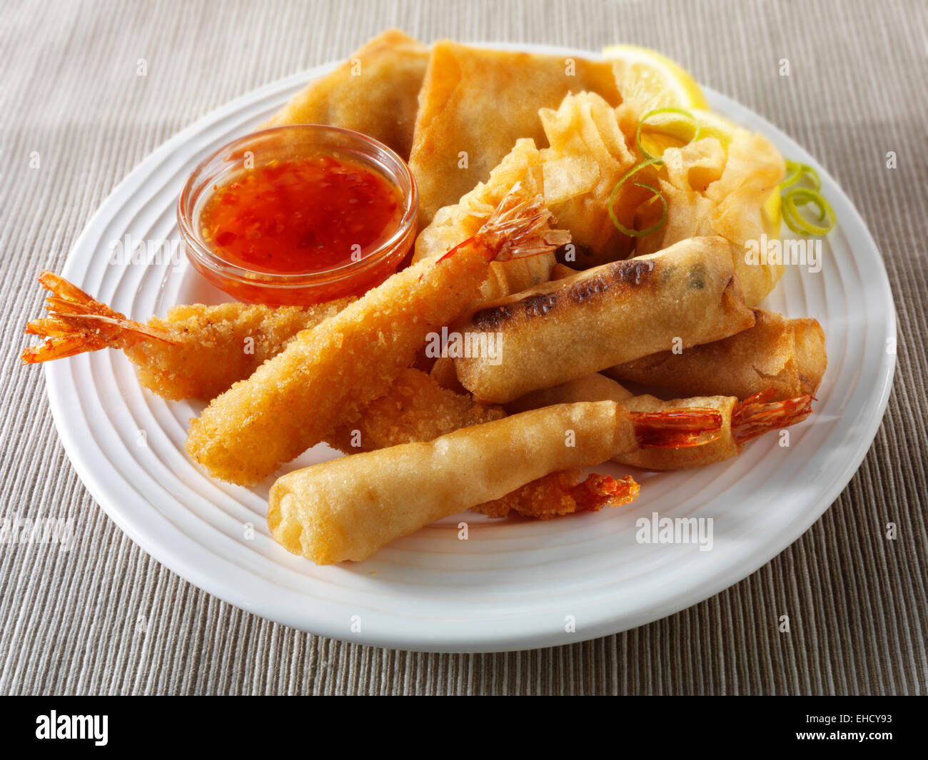 Cooked mixed Chinese starters - Dim sum, breaded prawns, spring rolls with chilli sauce served on a white plate Stock Photo