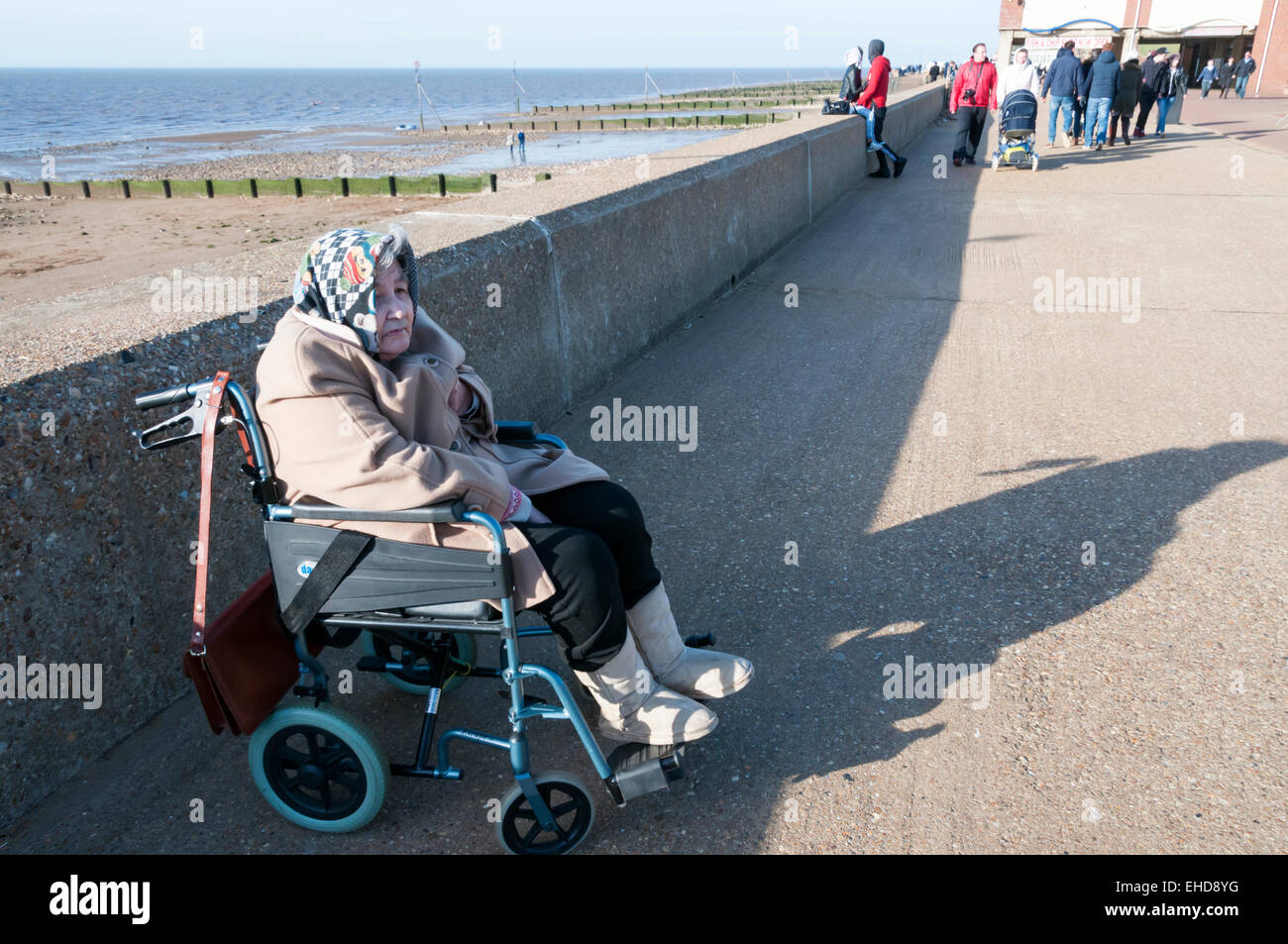 An elderly lady in a wheelchair keeps warm in the winter sunshine on Hunstanton promenade. MODEL RELEASED. Stock Photo