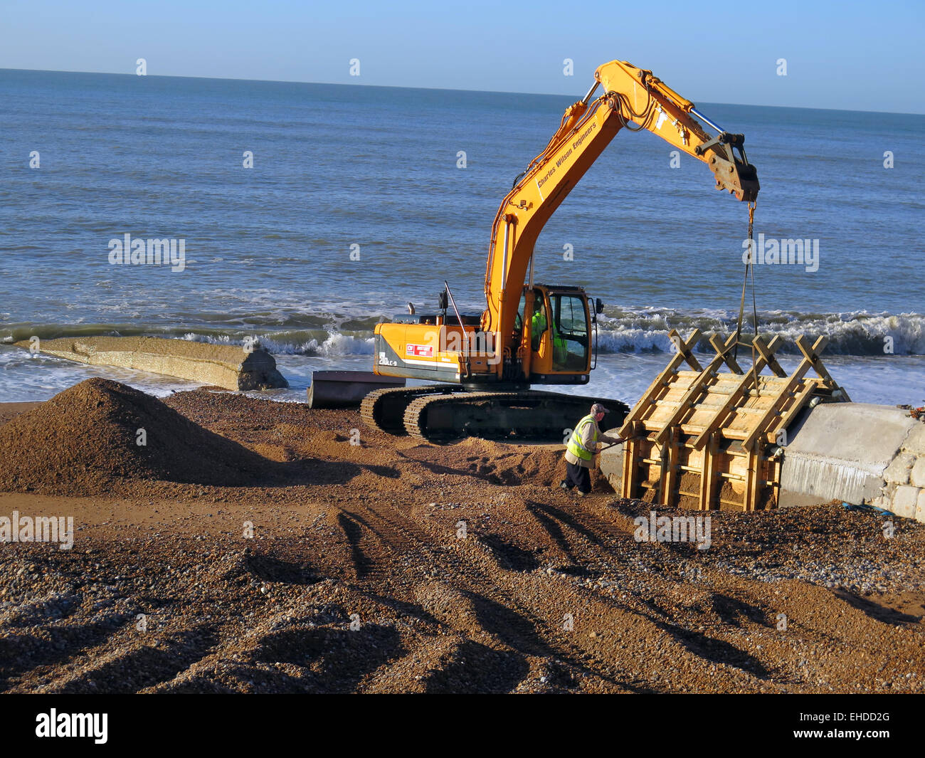 A Caterpillar Digger and Thorne Civil Engineering workers prepare to remove wooden moulding from new concrete Groynes being built on Hove beach, East Sussex. Stock Photo