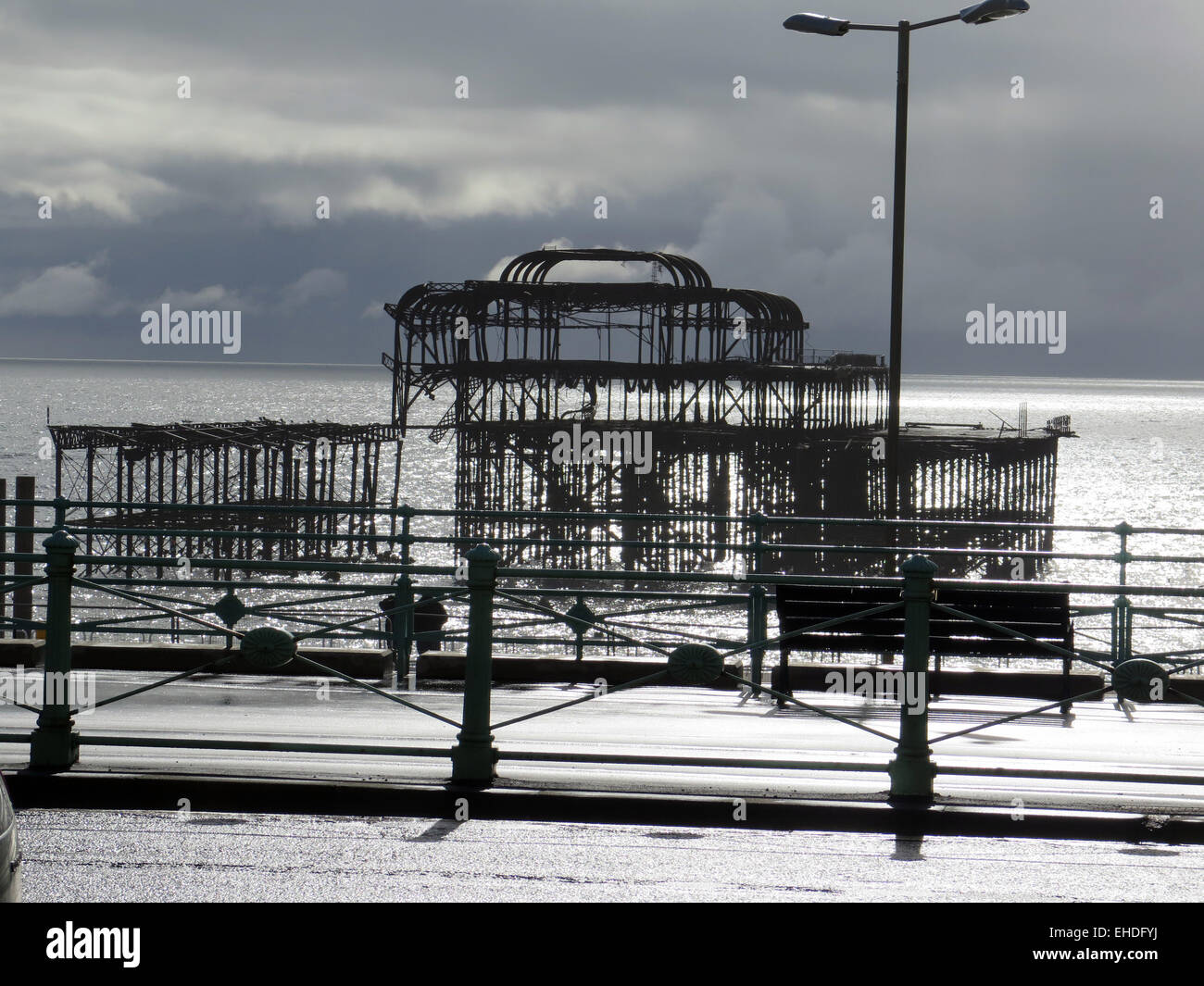 The Arson attacked ruin of the West Pier, Brighton designed by Eugenius Birch, seen across the promenade with decorative railings and benches to a glistening sea, and Cirrocumulus clouds. Stock Photo