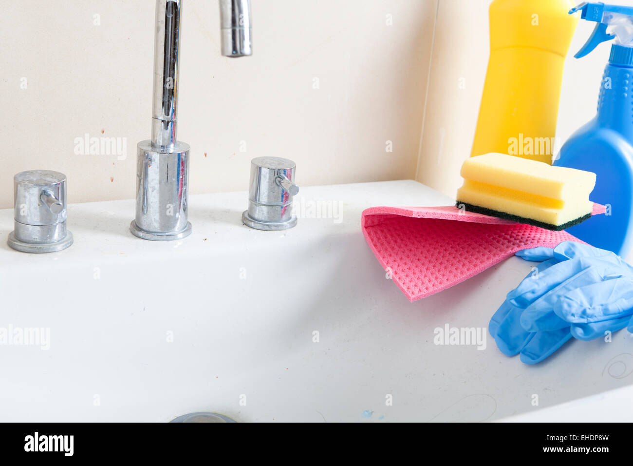 a dirty and calcified sink with cleaning gloves and cleaning products