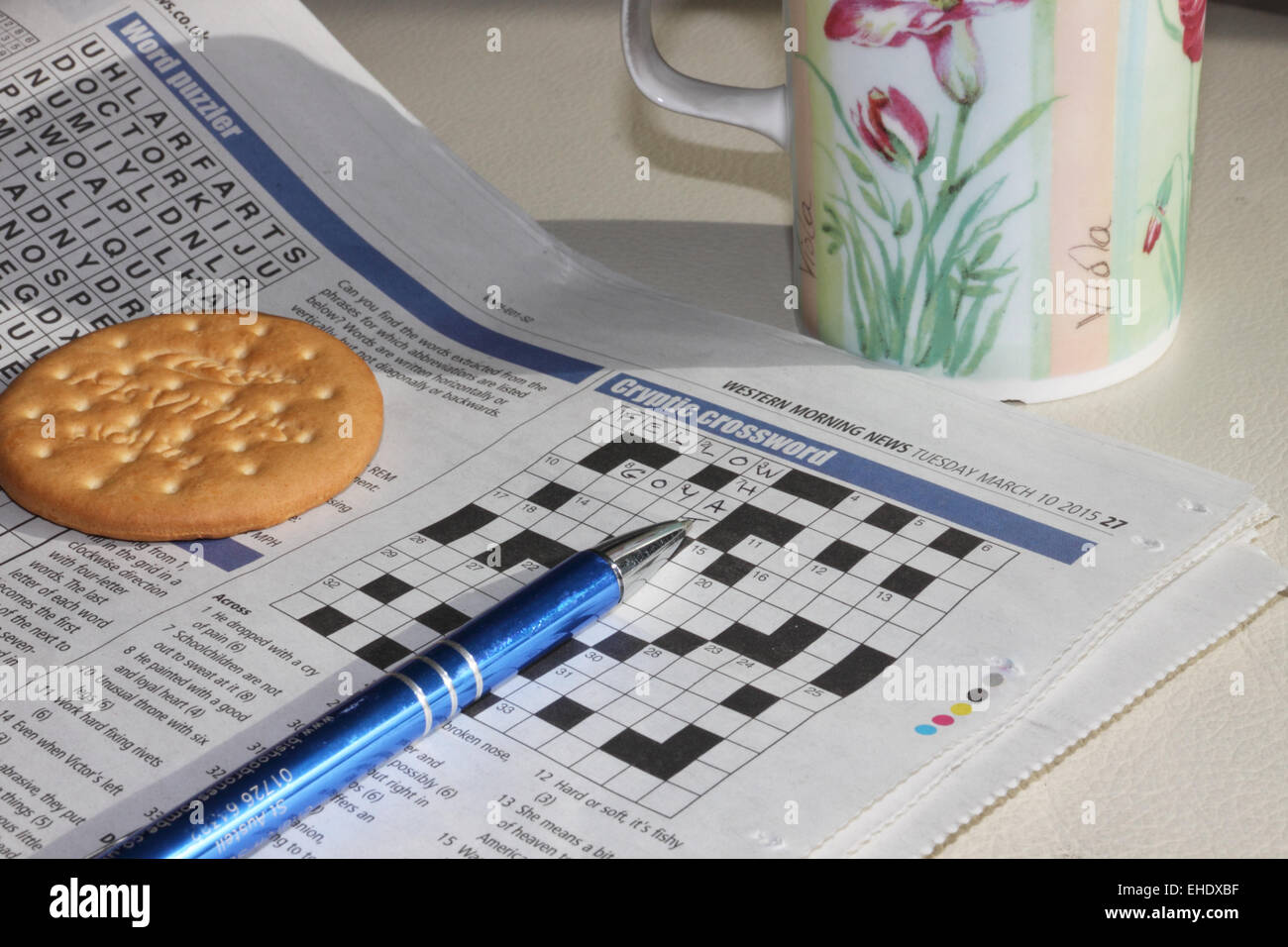 A newspaper open at the crossword page with a pen, mug and biscuit. Stock Photo