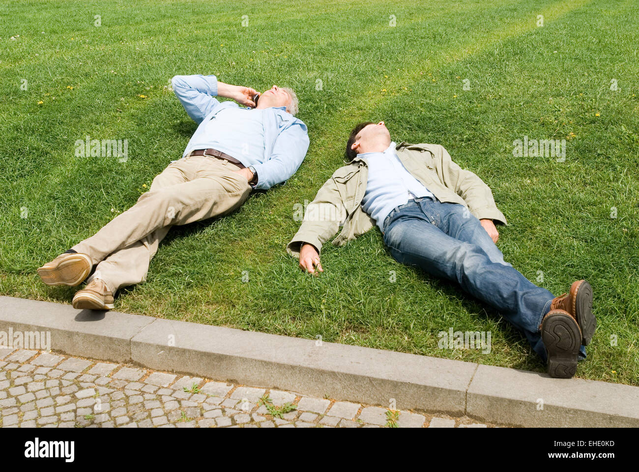 Two men enjoying first warm sunny day in the park sleeping and telephone Stock Photo