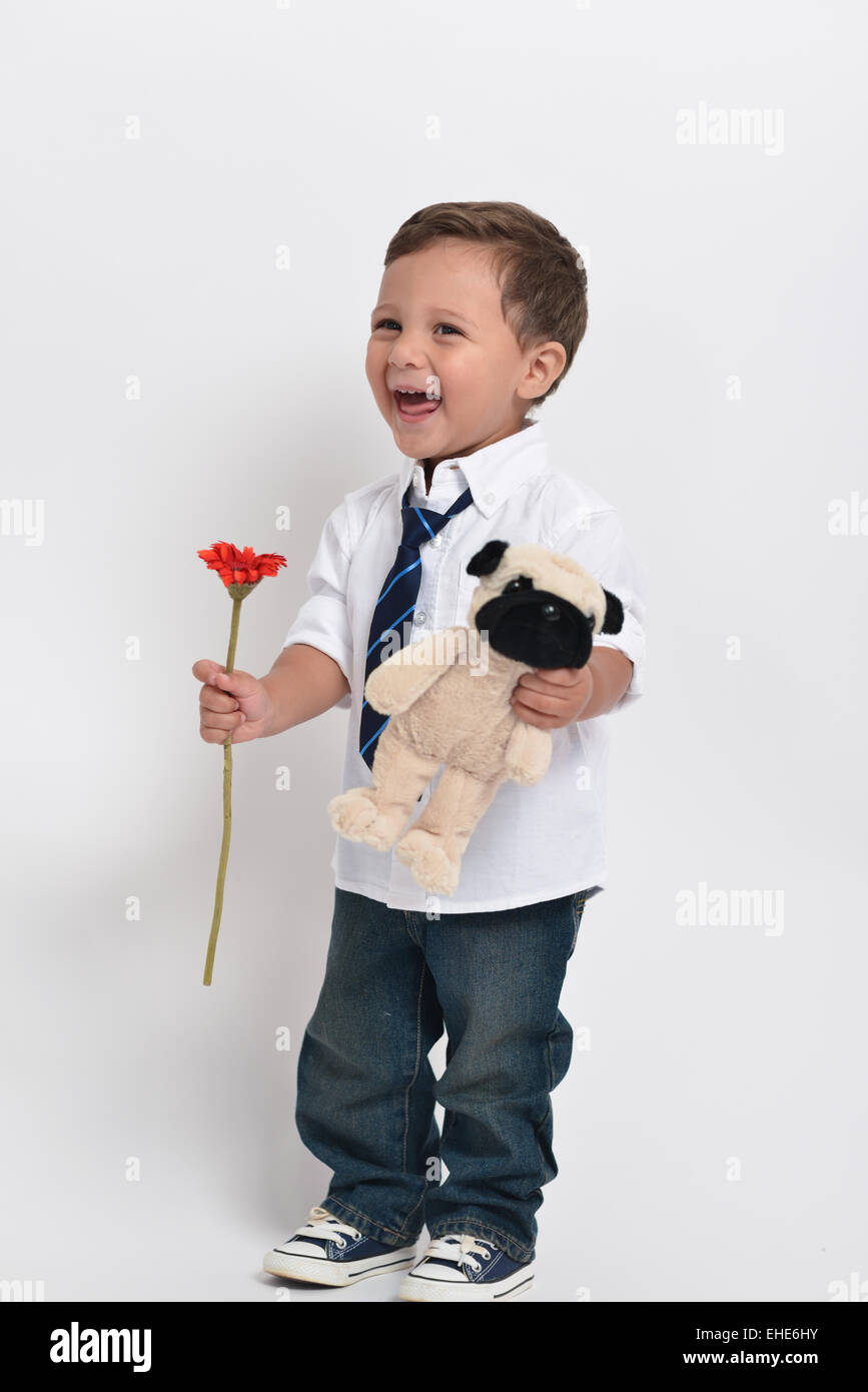 Two year old adorable toddler holding a flower and a stuffed animal - isolated in a white background. Stock Photo
