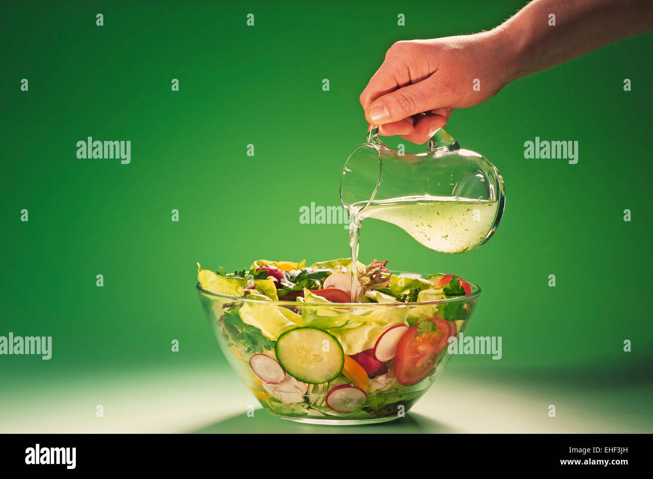 Hand pouring herbal vinegar into a bowl filled with salad Stock Photo