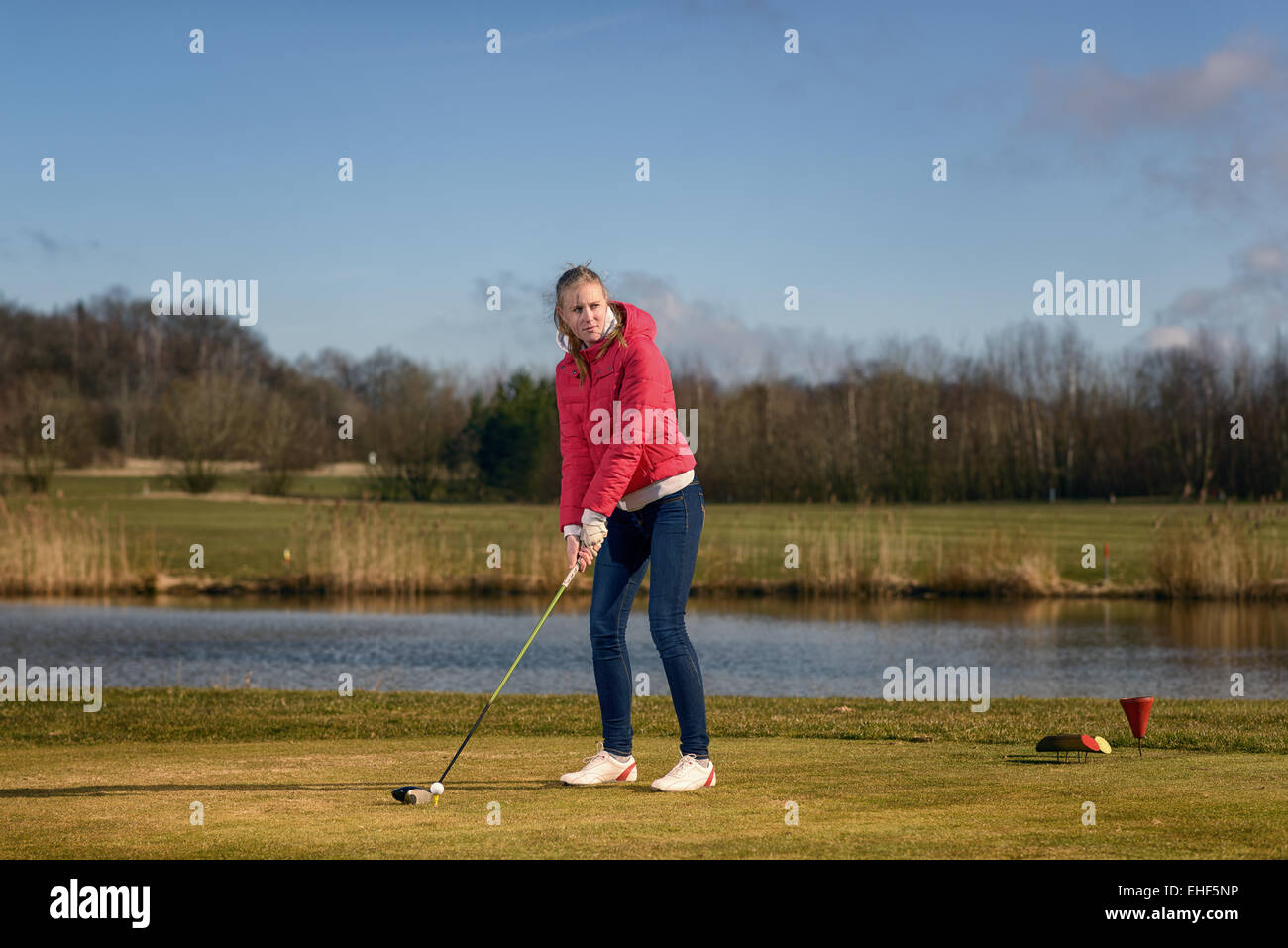 Woman teeing of on a golf course standing in the tee box in front of a water hazard with a driver in her hands ready to tee-off Stock Photo