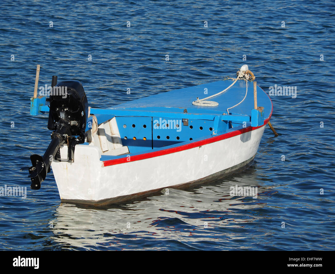 small wooden barge boat with outboard engine floats through blue lagoon waves Stock Photo