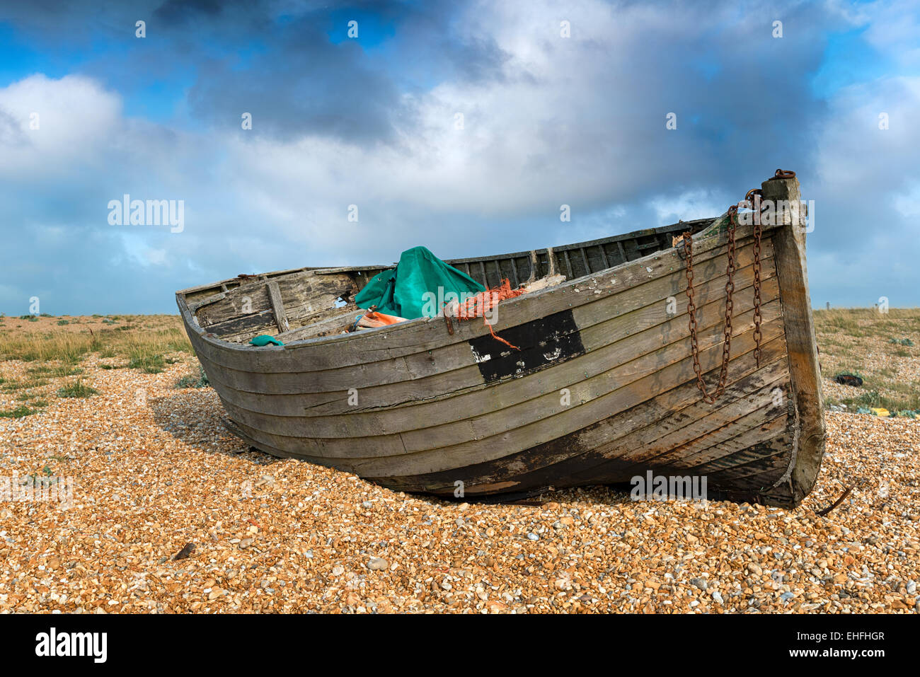 An old weathered wooden fishing boat under a blue sky on a shingle ...