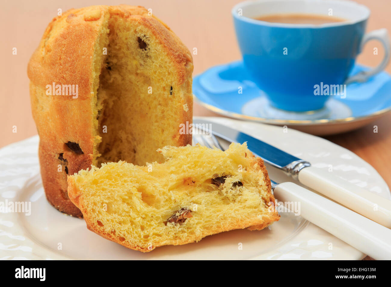 A slice of Panettone Italian Christmas fruit bread cake on a plate with a cup of tea on a table top. England UK Britain Stock Photo