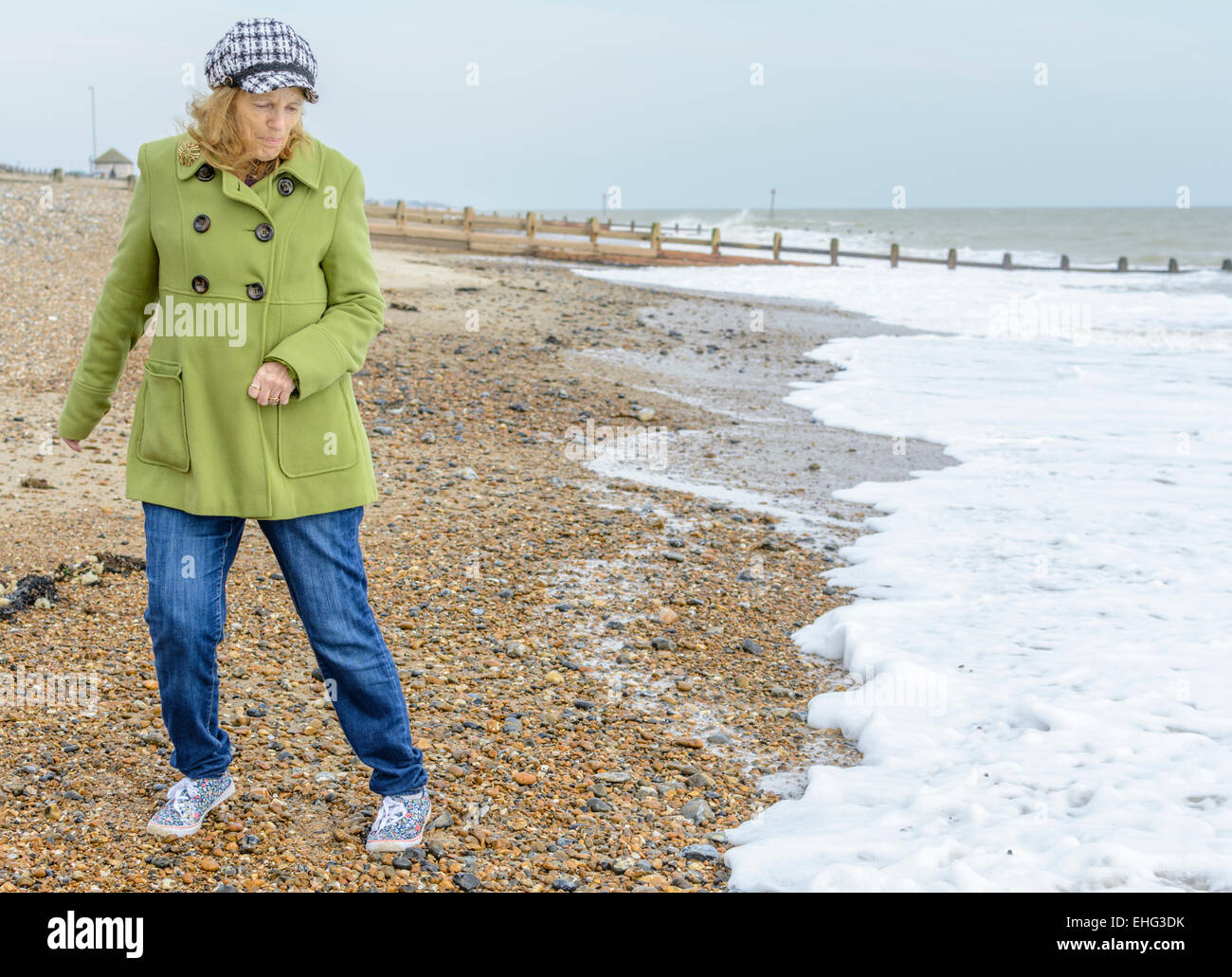 Middle aged woman dodging waves on a beach by the sea. Stock Photo