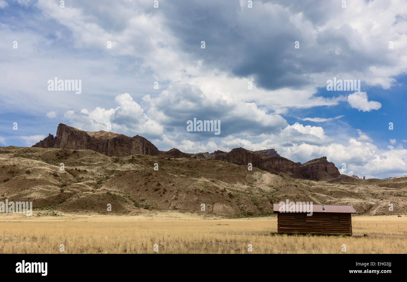 Isolated Log Cabin Flanked By High Rocky Mountains And Grassland