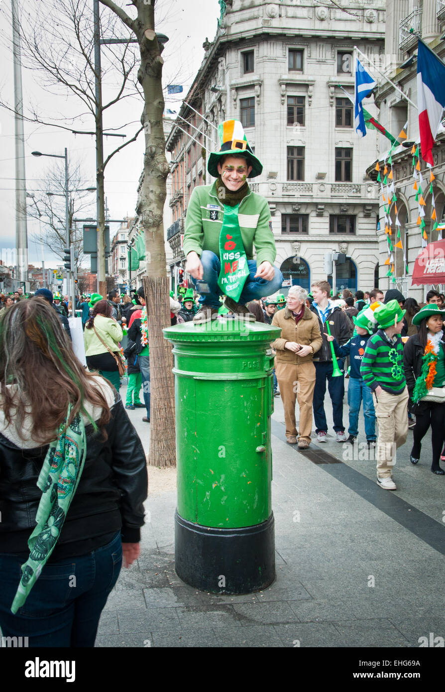 Tourist man dressed in green with leprechaun hat sits on green post box in O Connell Street, Dublin, Ireland, on St Patricks Day Stock Photo