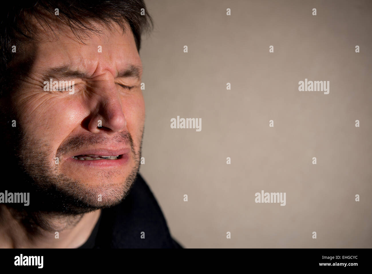 Close up of unshaven man, his eyes are closed and tearful, suffering from emotional pain. Stock Photo