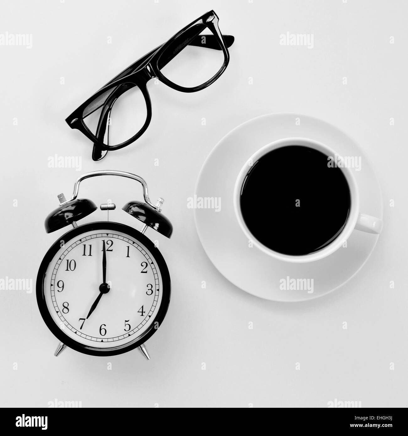 high-angle shot of a white table with a pair of black plastic-rimmed eyeglasses, and alarm clock and a cup of coffee Stock Photo