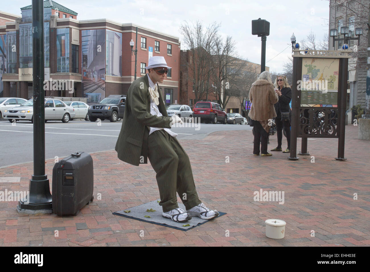 A living statue street performer makes tips as a man in a suit being blown backward at an impossible angle in Asheville, NC Stock Photo