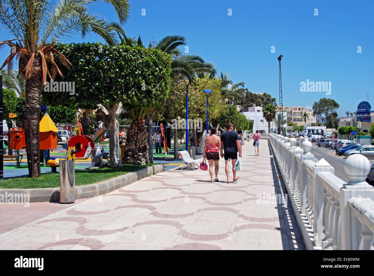 Tourists walking along the promenade with a childrens playground on the left hand side, Garrucha, Almeria Province, Spain. Stock Photo