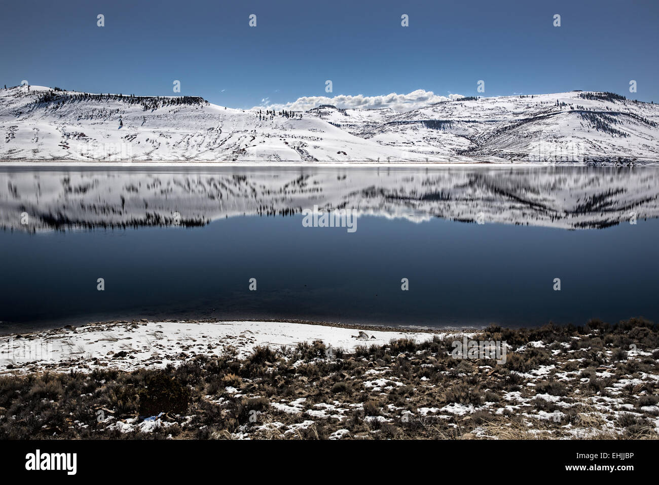 Reflection of snowy mountains surrounding partial frozen Blue Mesa Reservoir near Gunnison Colorado USA Stock Photo