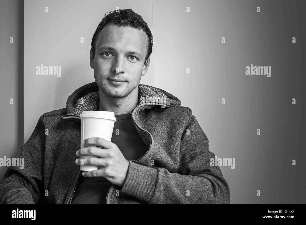 Portrait of young Caucasian man sitting in cafe with paper cup of Coffee. Black and white photo Stock Photo
