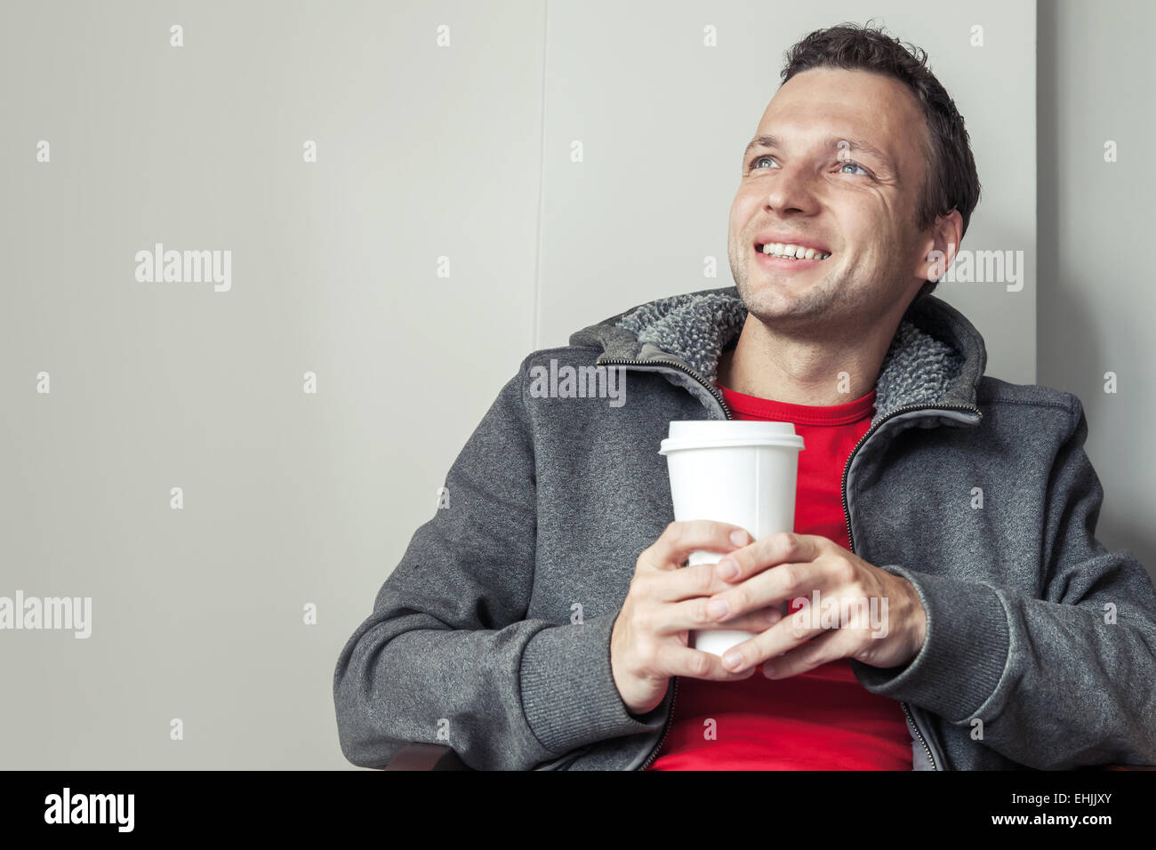Portrait of young Caucasian man sitting in cafe with paper cup of Coffee Stock Photo