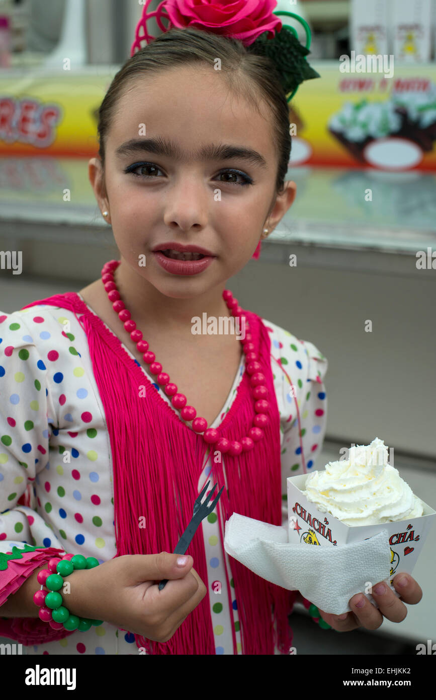 A girl in traditional attire enjoys an ice cream at the Fiesta de San Miguel in Orgiva, Andalucia, Spain Stock Photo