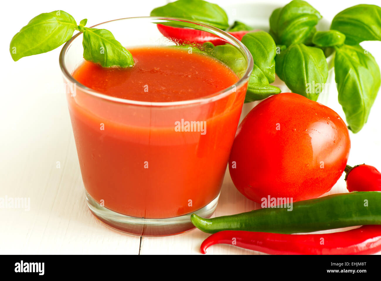 Tomato juice chili pepper and basil leaf on white wooden background