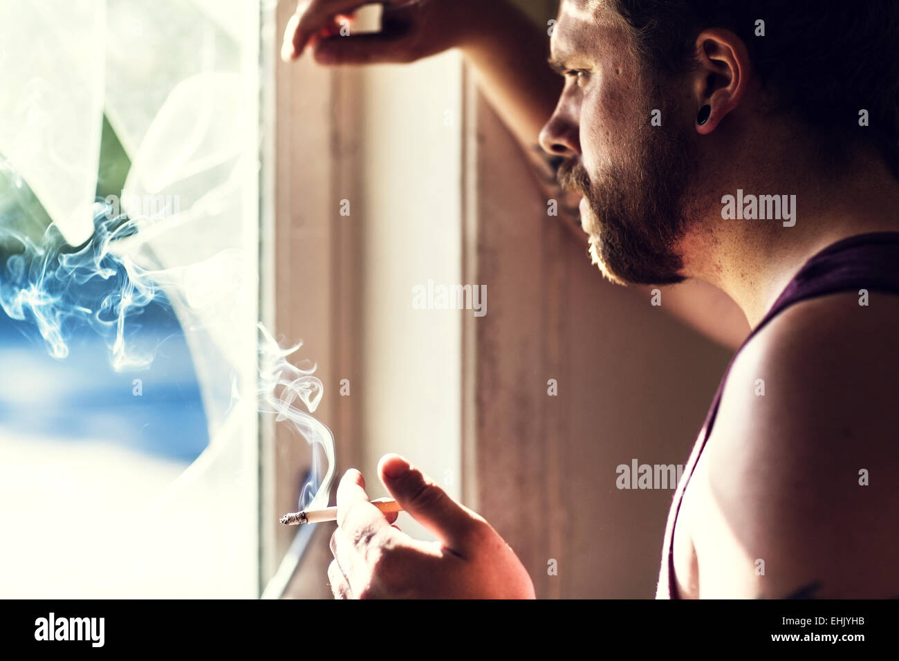 Rocker standing by a broken window, smoking cigarettes and thinking