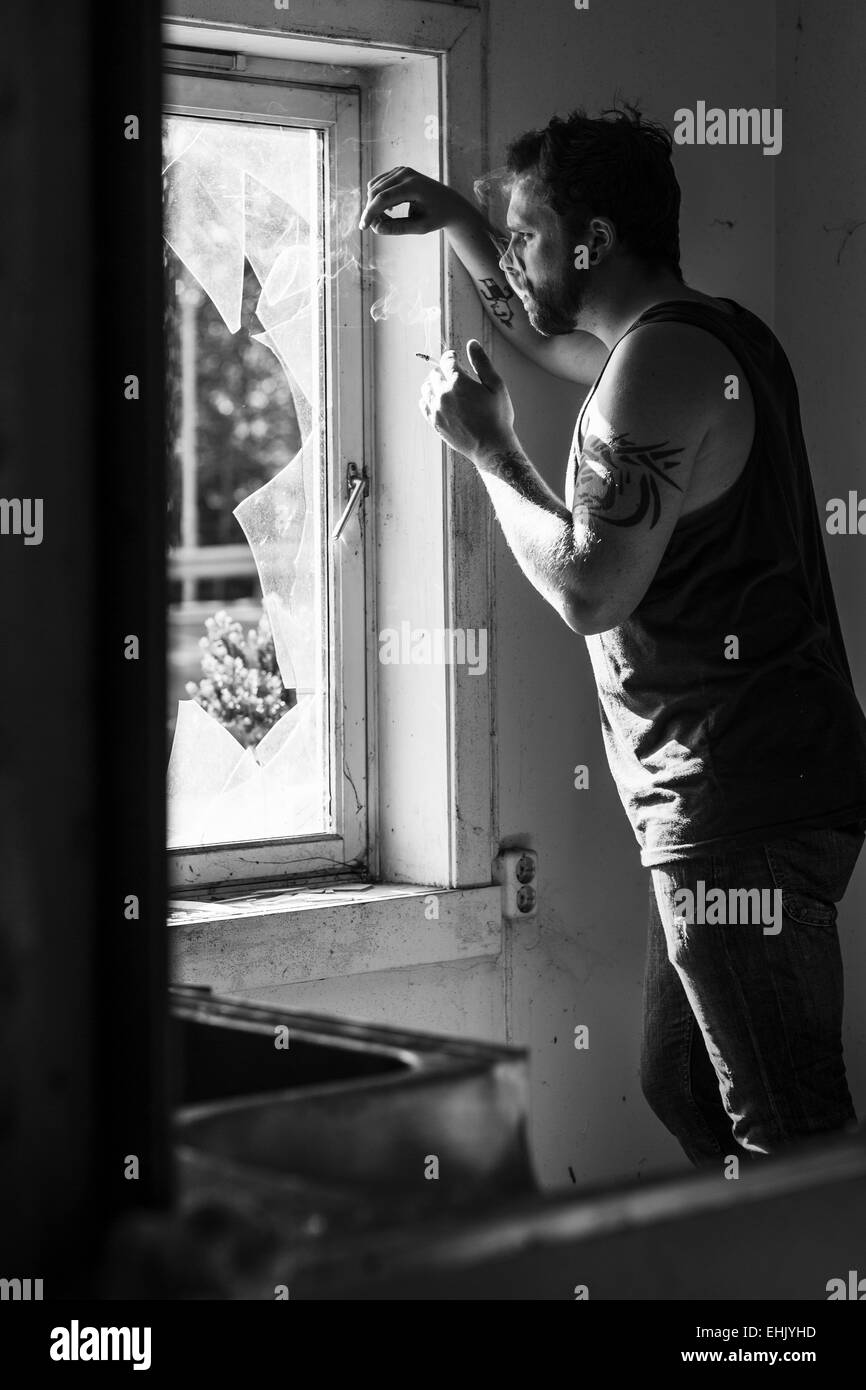Rocker standing by a broken window, smoking cigarettes and thinking