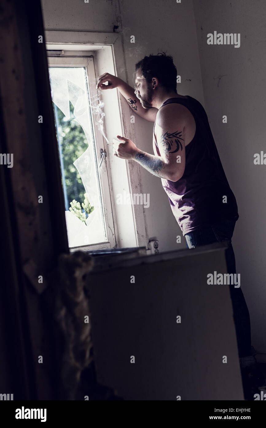 Rocker standing by a broken window, smoking cigarettes and thinking