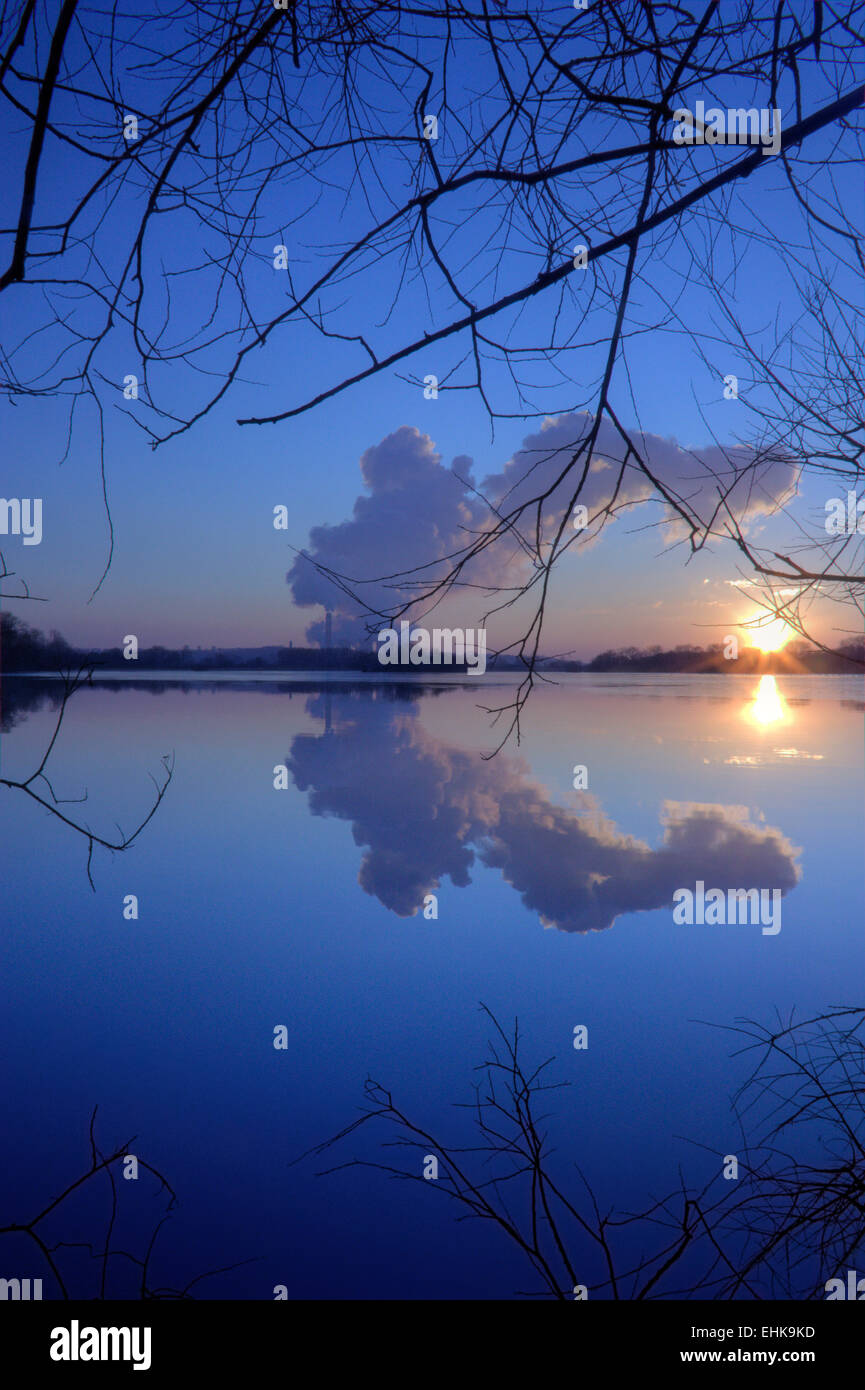 A power station releasing plumes of steam into the sky at sunset, reflected in the surface of a large pond. Stock Photo