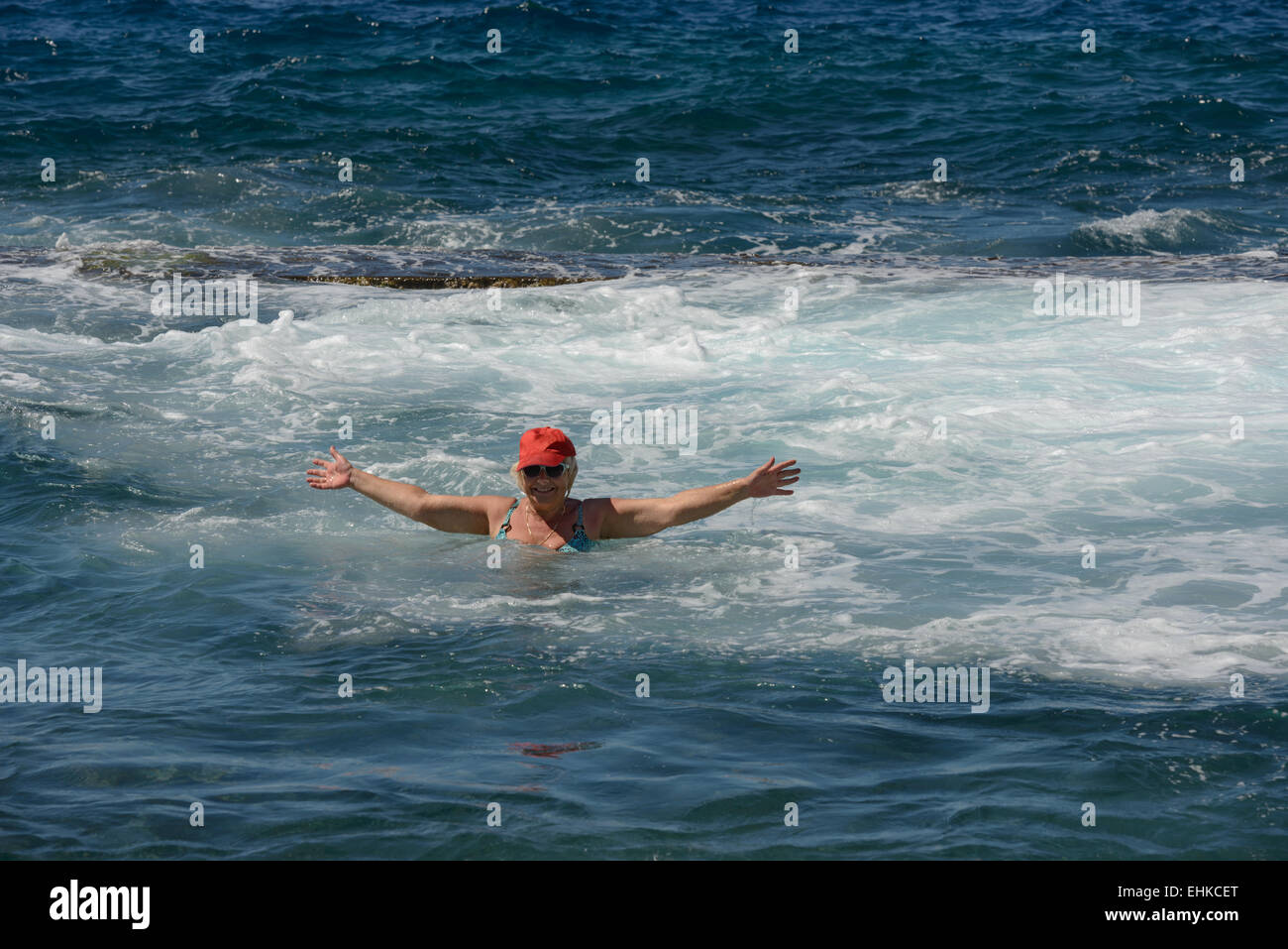Senior woman is bathing in the foam of the ocean surf. Stock Photo