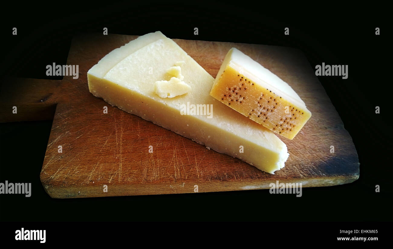 Slice of Parmesan on the chopping board on dark background. True genuine Italian Parmesan must have the name punched on its rind Stock Photo