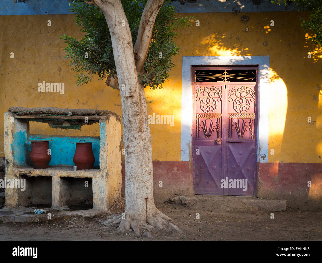 2 pottery public drinking water carriers on the roadside under a shady tree in front of yellow house and metal door Egypt Africa Stock Photo
