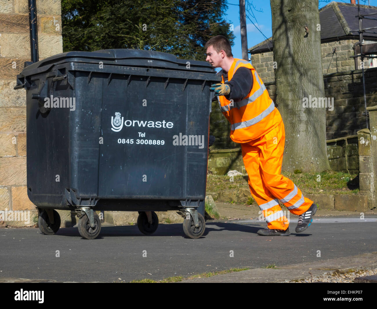 A Waste Disposal Operative in high visibility clothing pushing a commercial sized wheelie bin back to a café, after tipping. Stock Photo