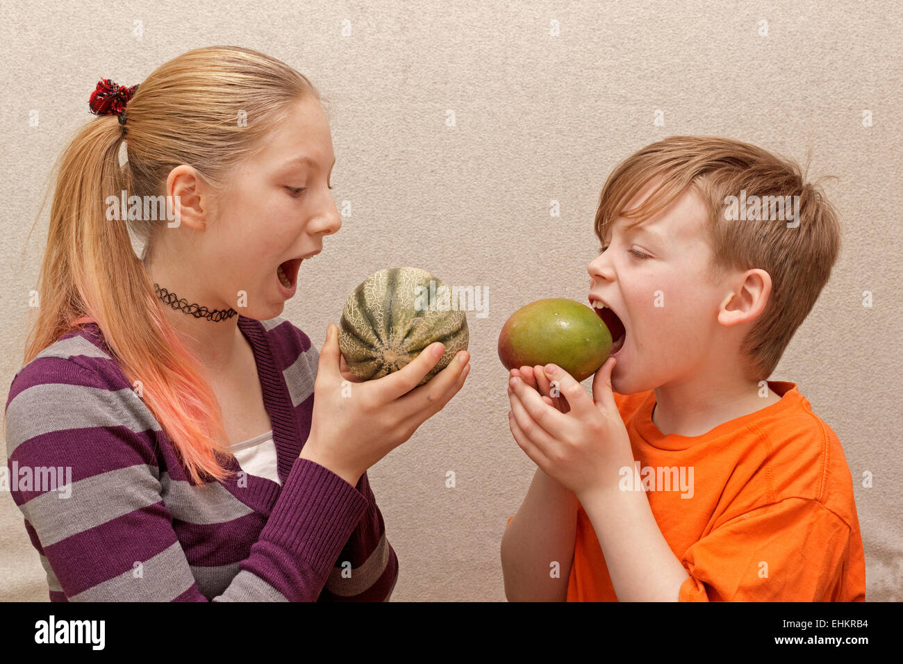 children pretending to eat unpeeled cantaloupe and papaya Stock Photo