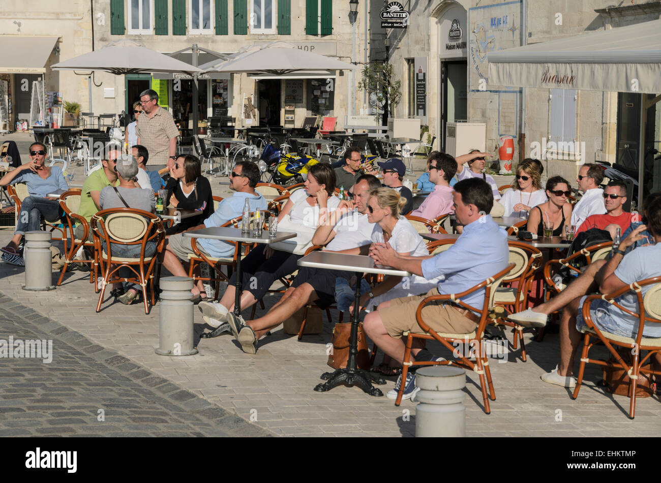 Locals and holidaymakers enjoying a drink in the sun at a cafe on the quayside at St Martin en Re, Ile de Re, France. Stock Photo