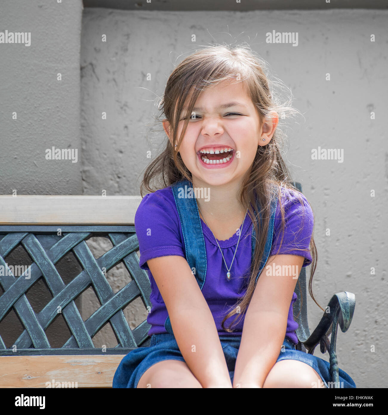 Little girl sits laughing on outside bench. Stock Photo