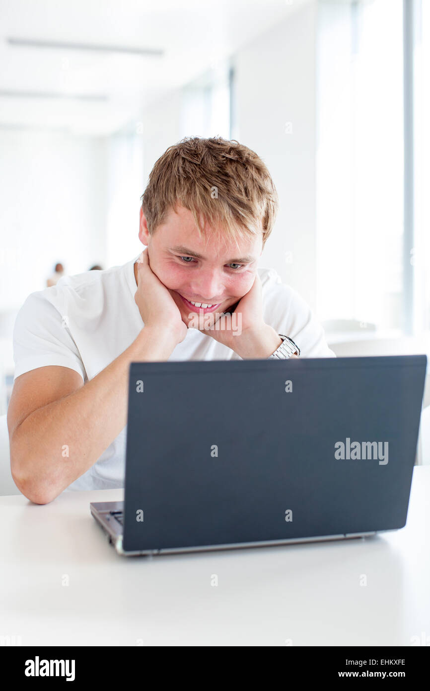 Handsome male student using a computer in a university library/study ...