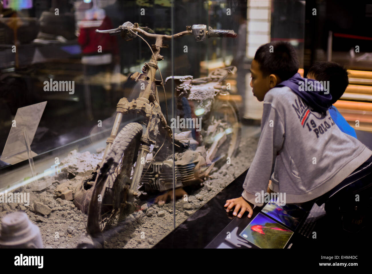 Bandung, Indonesia. 15th Mar, 2015. Children observe a damaged motorcycle hit by pyroclastic flows, at Geology Museum, Bandung, Indonesia. The artifact was taken from 2010 Mount Merapi eruption site in Yogyakarta province. Stock Photo